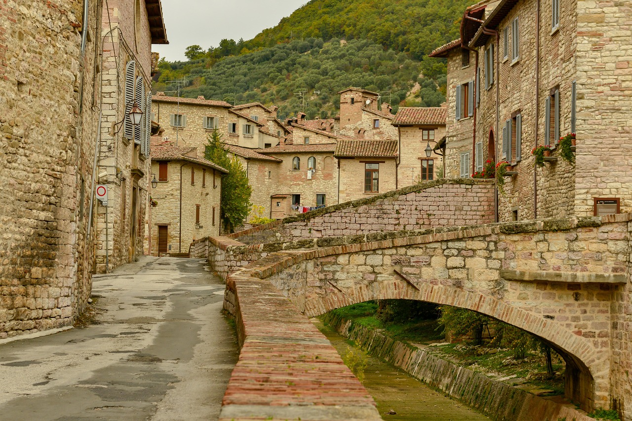 Vista del borgo umbro con torrente centrale e passerella di legno che collega le due sponde.